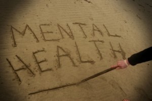 A young man suffering from depression writes the words mental health in the sand